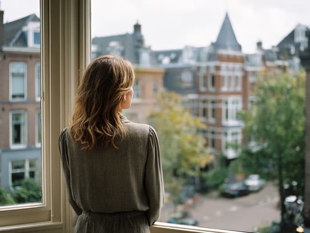 Iemand kijkt vanuit een lichte woning uit over de daken van de straat